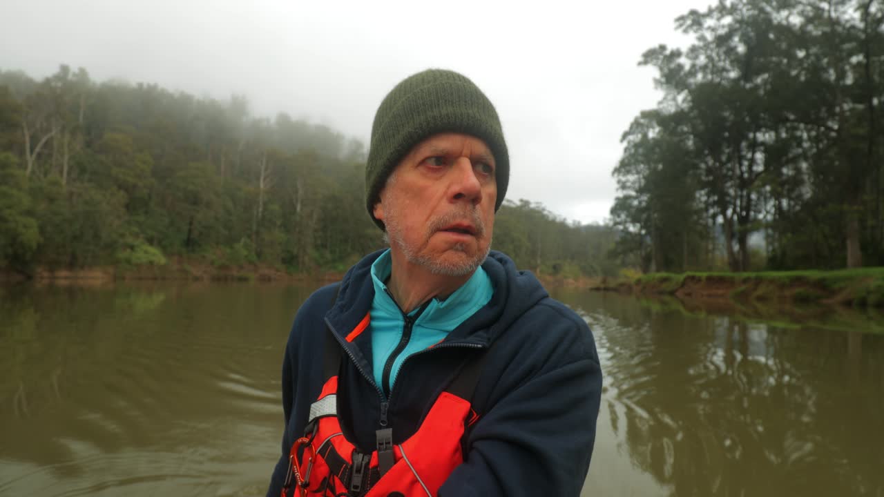 hombre viejo remando en canoa por el río bordeado de árboles brumosos