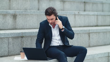 Businessman-working-on-laptop-computer-at-street.-Manager-talking-on-smartphone