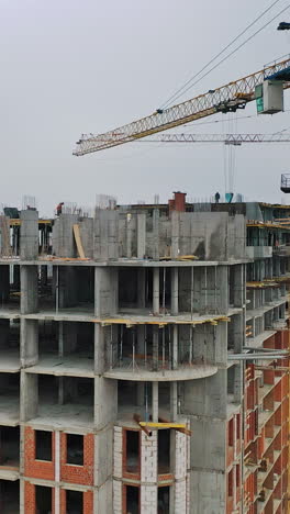 new construction site in the city. two big cranes constructing the urban building. construction of high-rise building on the city background. aerial view. round motion of camera. vertical video