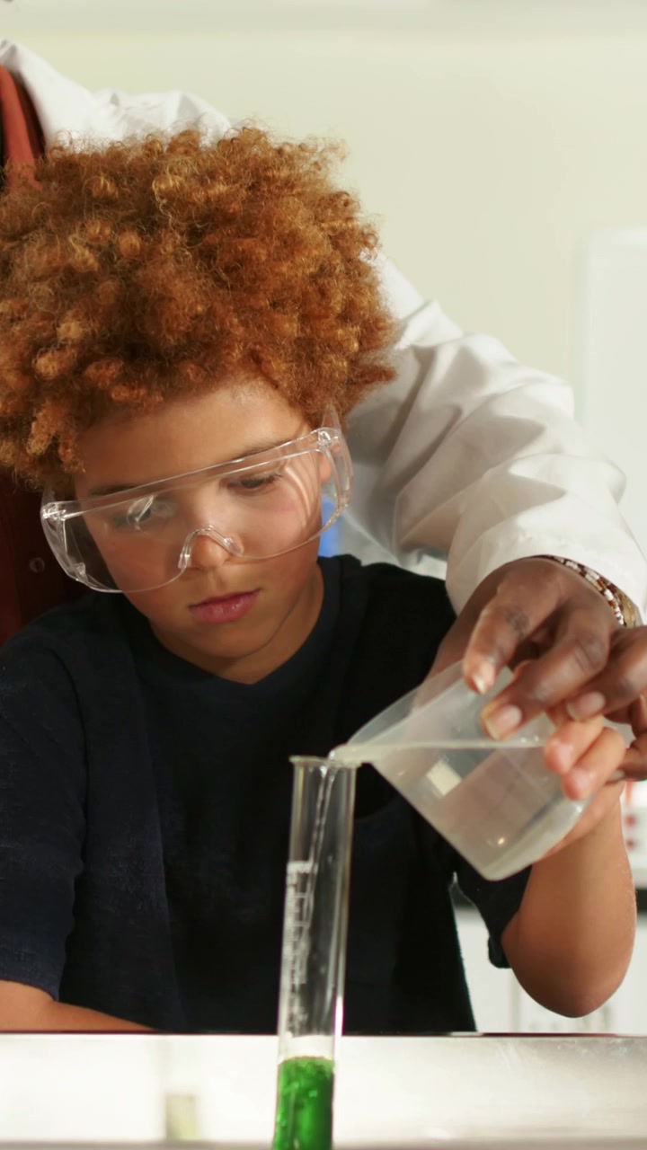 Vertical video: Watching child wearing goggles as adult pouring green fluid into cylinder