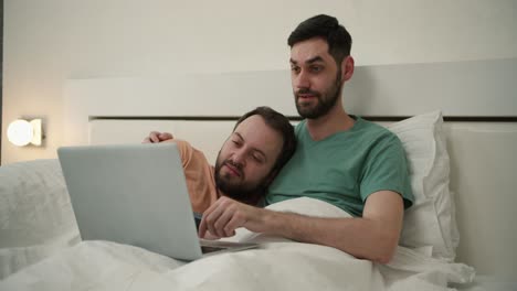 pareja de hombres homosexuales pasan tiempo en casa acostados en la cama, usando computadora portátil