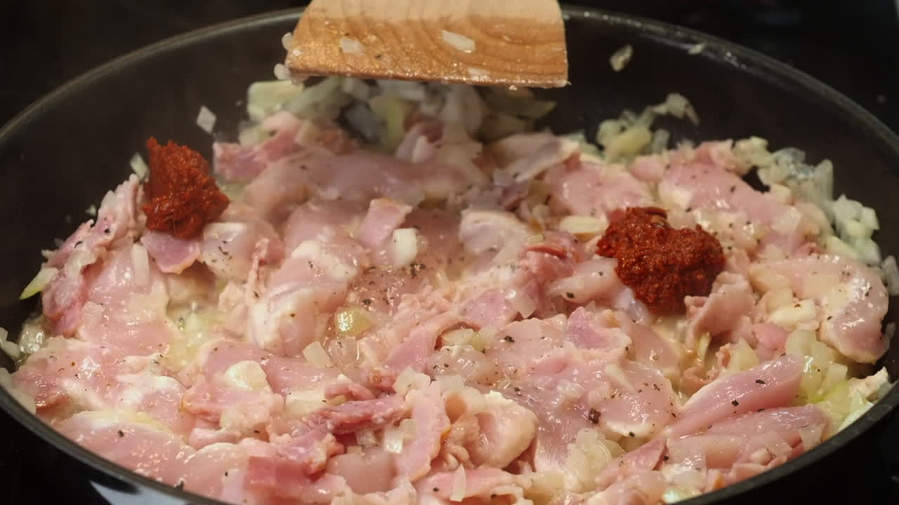 Spoonfuls of curry paste added to chicken and onions in cooking pan