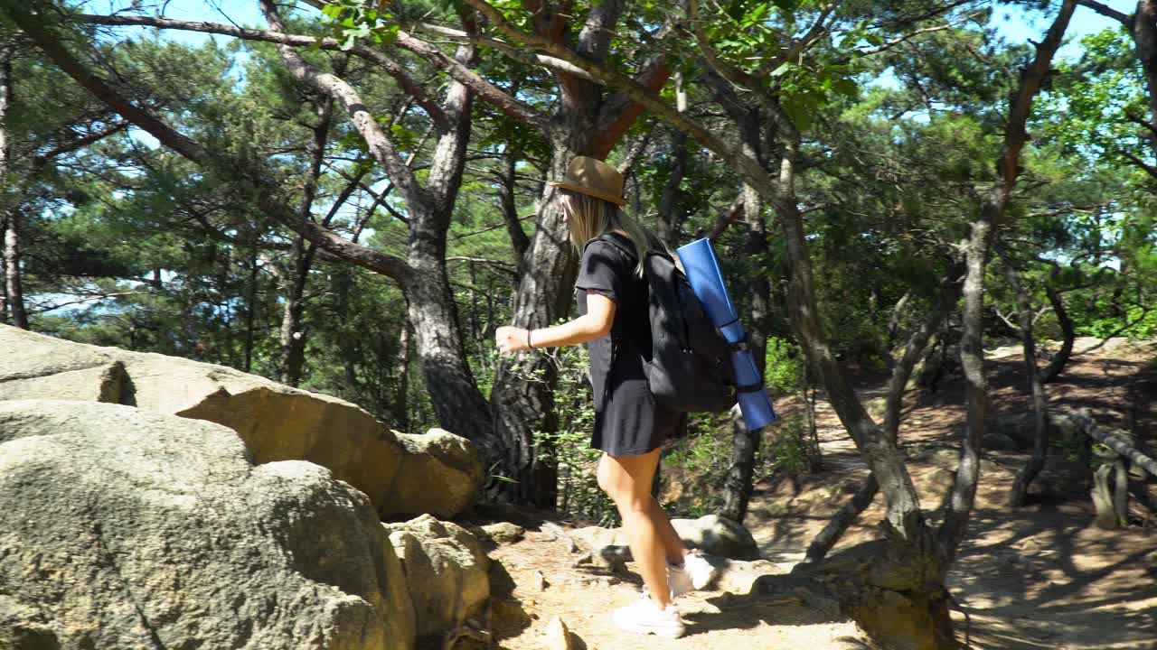 chica caucásica con mochila y colchoneta de yoga caminando y escalando rocas en un día soleado junto a la montaña gwanaksan en seúl, corea del sur