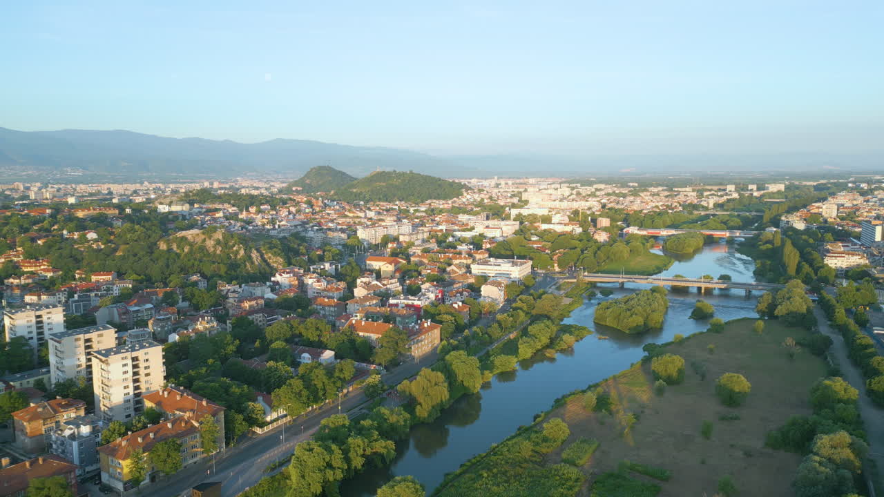 Drone footage of Plovdiv and the Maritsa River during sunrise in early spring. The soft morning light reveals bridges, cityscape, and lush greenery across Bulgaria’s second largest city