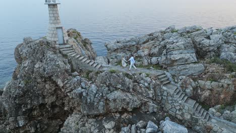 isla de kalamota, mar adriático, croacia - una pareja dirigiéndose hacia el faro para apreciar la puesta de sol - toma aérea de retroceso