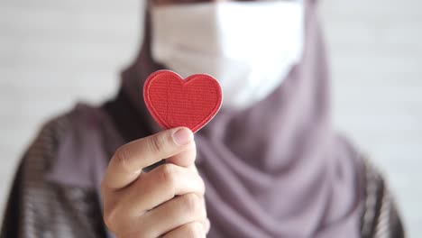 woman in hijab and mask holding a red heart