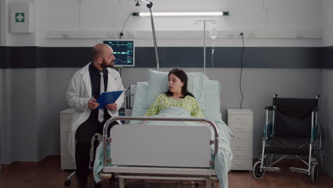 Front-view-of-sick-woman-resting-in-bed-discussing-with-oncologist-man-doctor