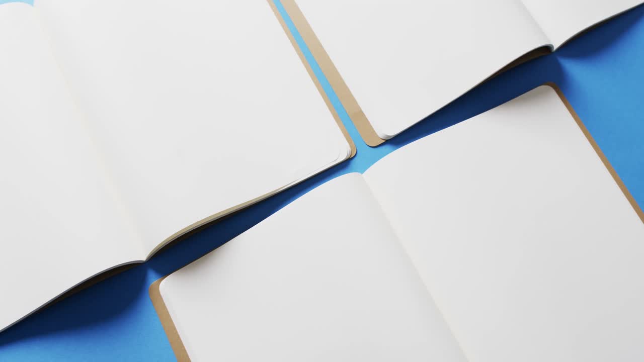 Close up of open blank books with copy space on blue background in slow motion