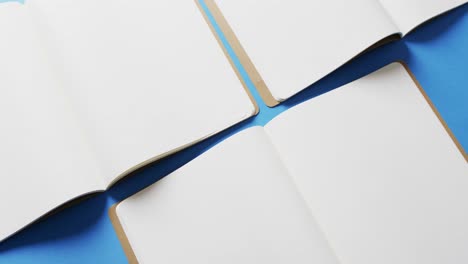 Close-up-of-open-blank-books-with-copy-space-on-blue-background-in-slow-motion