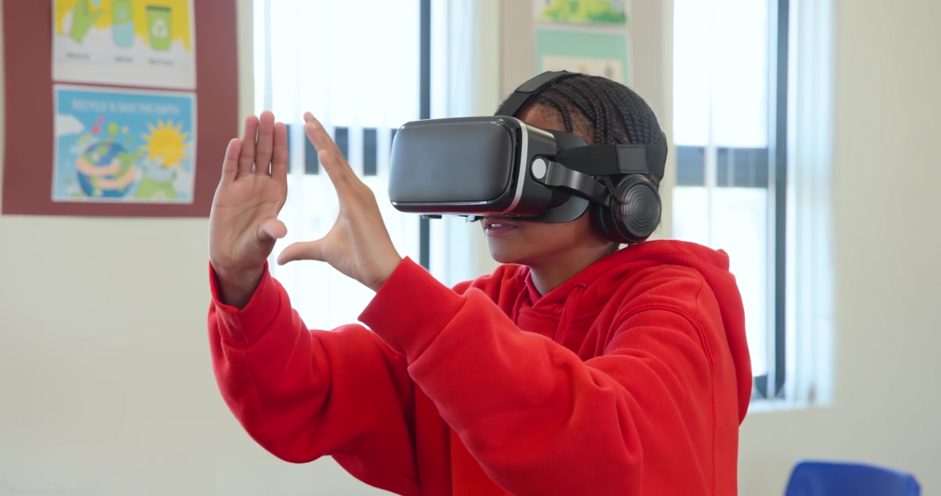 Adolescente afroamericano con visore VR e felpa rossa con cappuccio, che gesticola e manipola l'interfaccia utente VR in classe