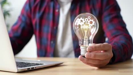 man holding a glowing lightbulb with gears inside representing a new idea