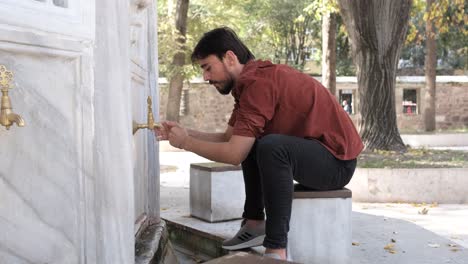 back view of muslim bearded man performing ablution, man washing his arms and elbows at mosque fountain