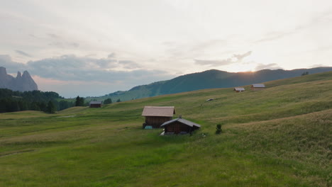 drone reveals solitary hut in open alpe di siusi field with dolomite peaks beyond