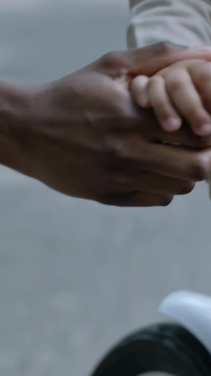 Vertical video: Reaching adult forearm in light coat calming small hand at park releasing, smiling