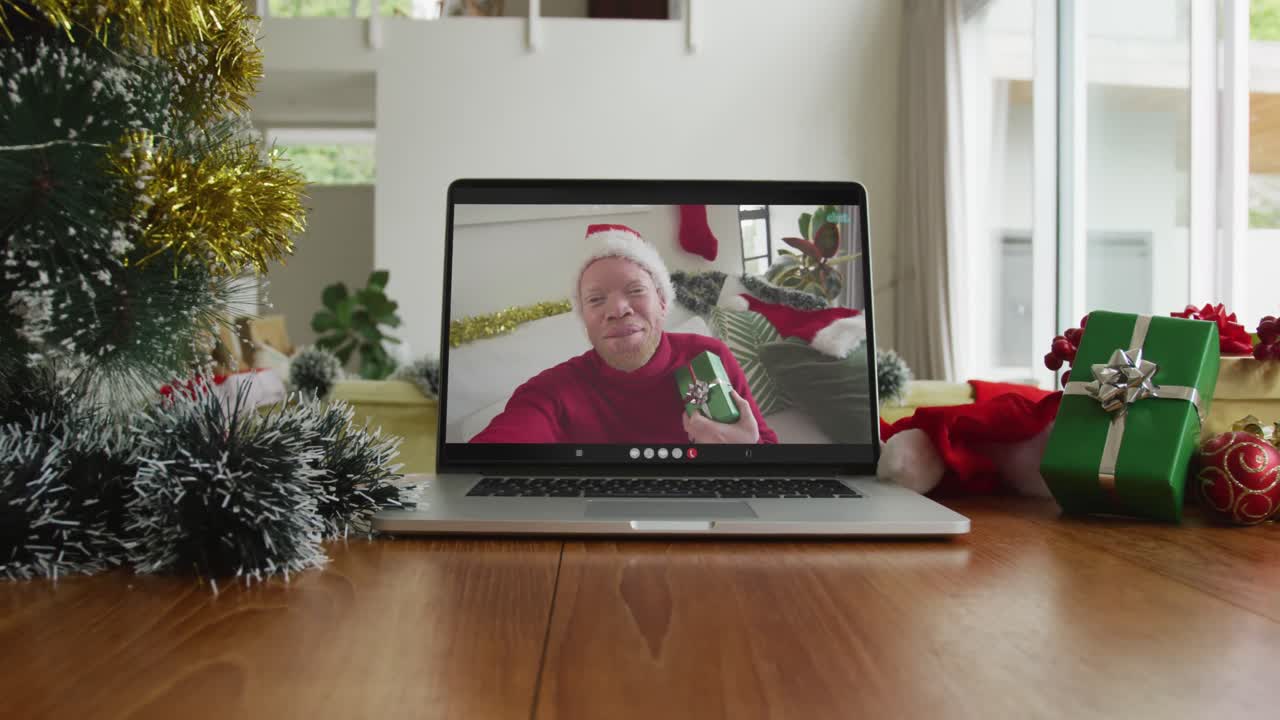 hombre afroamericano albino sonriente con sombrero de papá noel en una videollamada en una computadora portátil