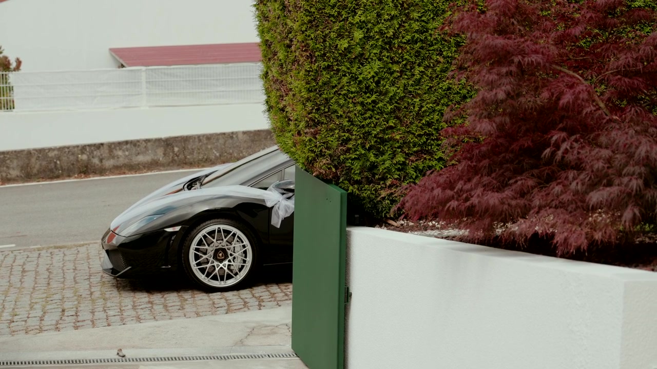 Lamborghini nera decorata con un nastro parcheggiata su un vialetto di ciottoli