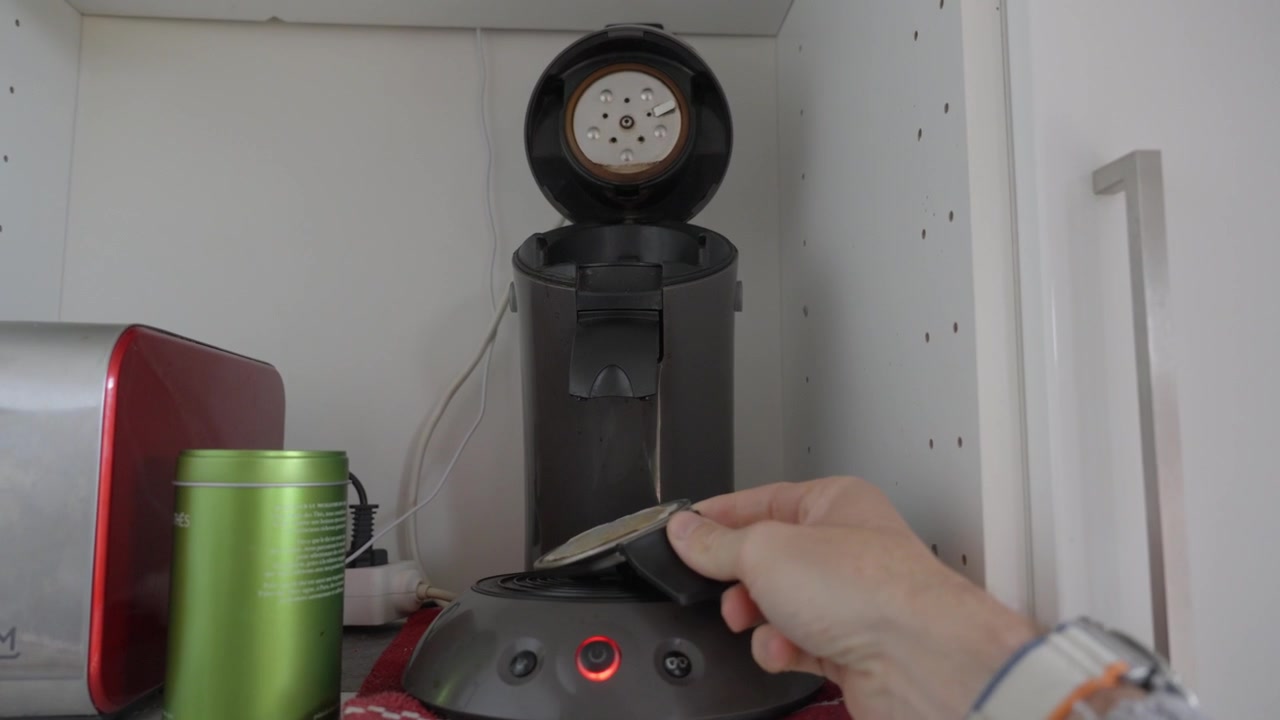 POV Primo piano di una mano che preme il pulsante per avviare una moderna macchina da caffè a capsule in cucina