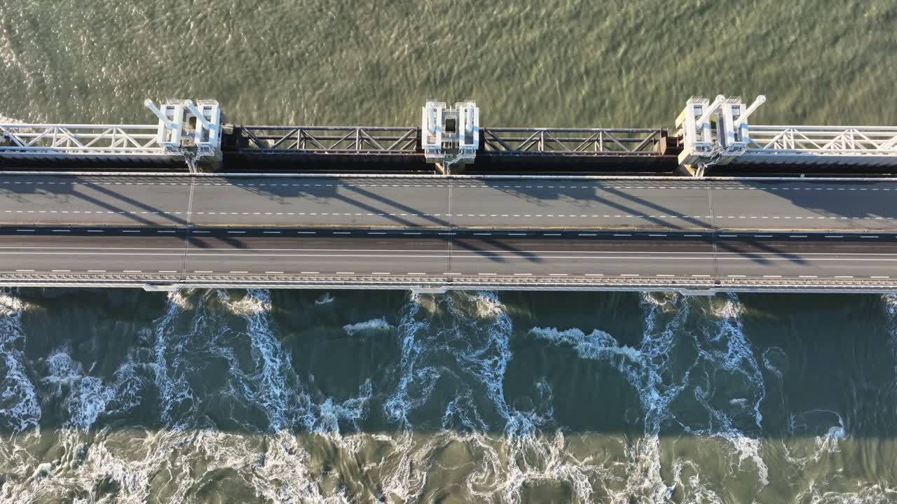 tiro de inclinación vertical aérea de agua que fluye a través de esclusas abiertas en la barrera de marejada de tormenta scheldt oriental en zelanda, los países bajos, en un día soleado