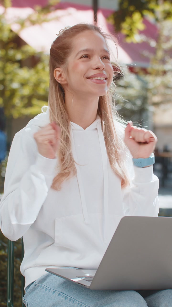 Una donna freelance felice che lavora sul portatile urla di trionfo, celebra il successo seduta su una sedia.
