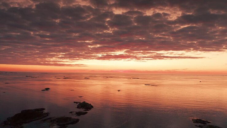 A serene aerial view of a water landscape and heavy clouds, highlighted by the dark orange light of the setting sun