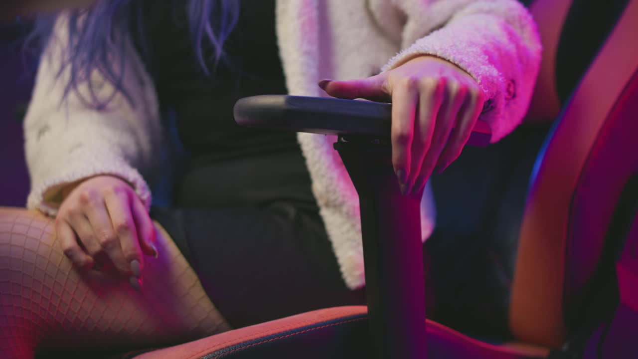 Close up woman adjusting reclining lever on gaming chair while seated in fluffy sweater and stockings under neon pink and purple lights, showcasing ergonomic comfort and relaxed posture in studio