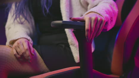 close up woman adjusting reclining lever on gaming chair while seated in fluffy sweater and stockings under neon pink and purple lights, showcasing ergonomic comfort and relaxed posture in studio
