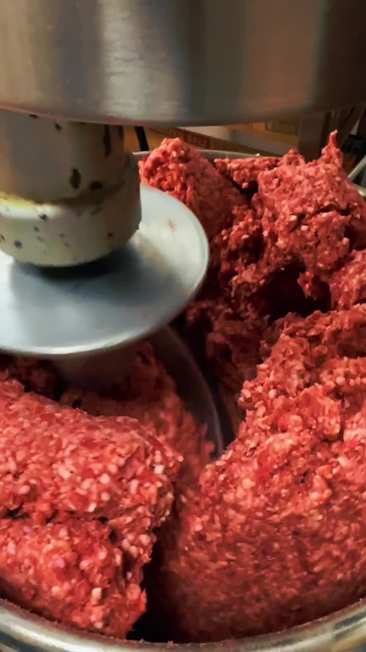 Industrial meat mixer processing raw ground beef in food facility. Large metal blade mixing fresh red minced meat in a commercial food processing machine with motion blur