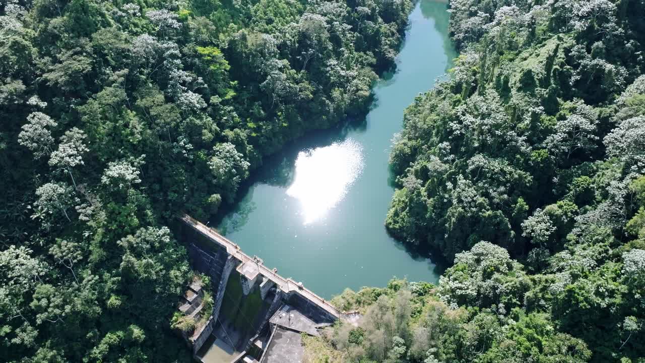 Aerial top down shot of Tireo Dam with green river and green nature during sunny day in Bonao, Dominican Republic