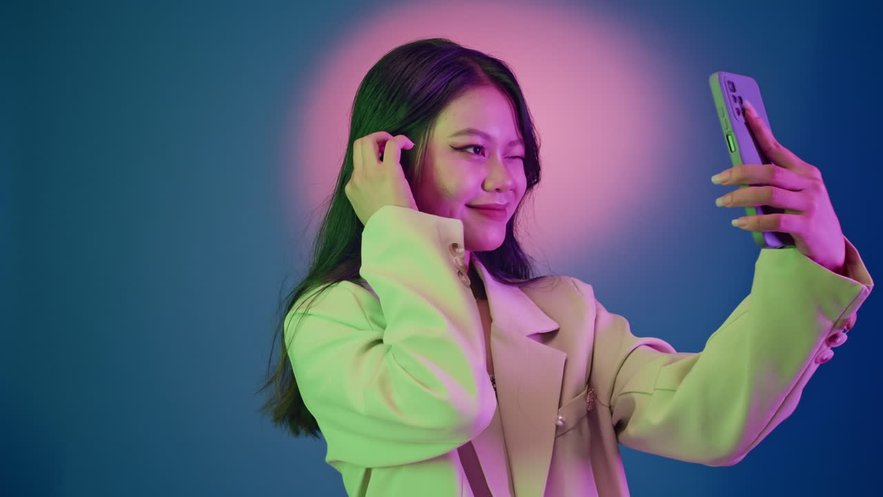 Asian Brunette Taking Selfies on Smartphone on Neon Background