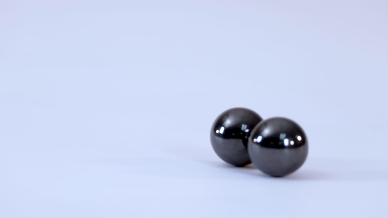 Close-up shot of two metallic magnetic balls rolling together and connecting on a white background