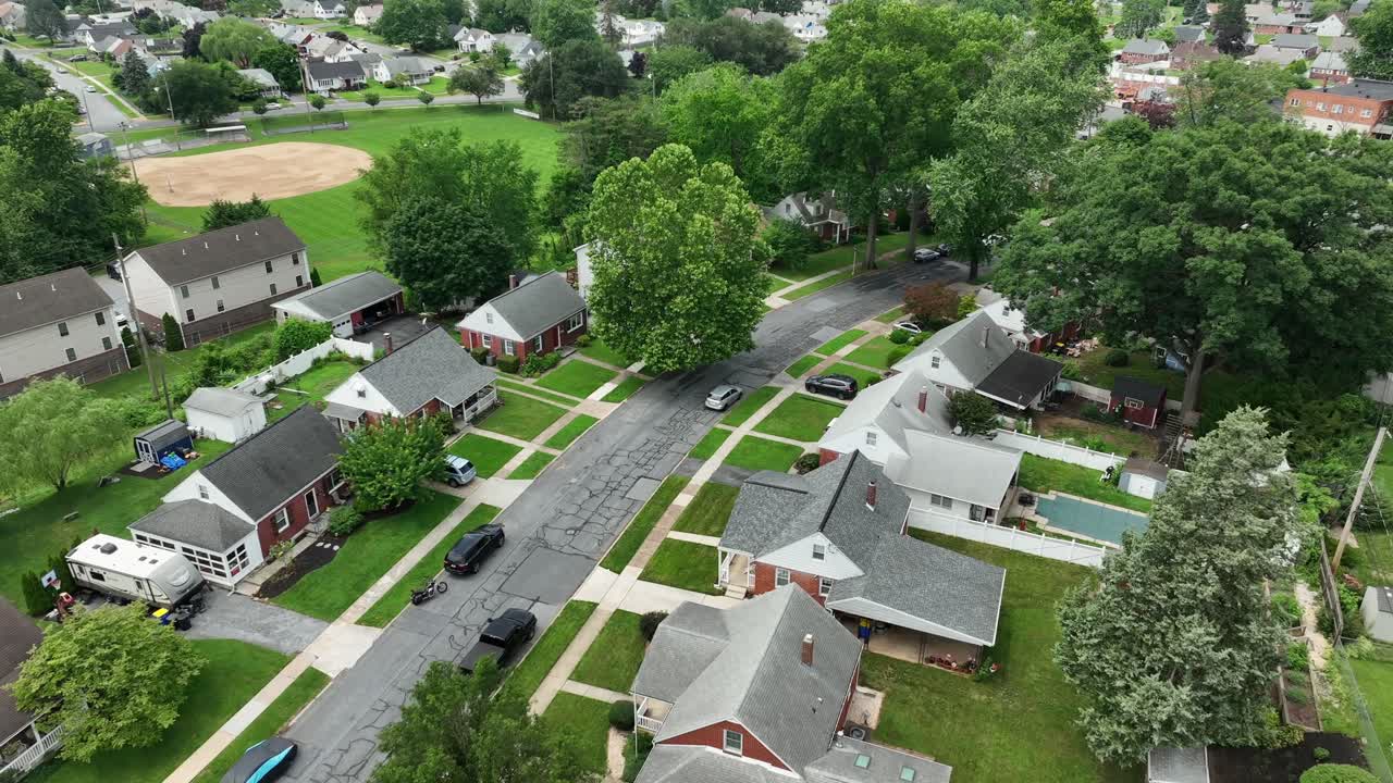Single family houses with red brick facade in suburb district of town. Green grass in garden. Quiet atmosphere. Aerial flyover shot. Middle class housing area of USA