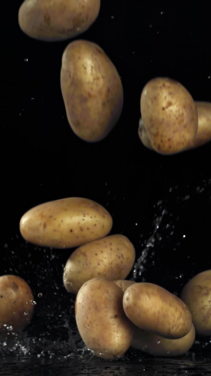 Patate fresche che cadono e schizzano acqua su sfondo nero al rallentatore
