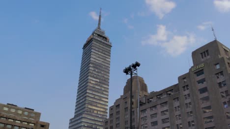 una amplia toma panorámica en cámara lenta de la torre latinoamericana y el palacio de bellas artes en la ciudad de méxico, con algunos turistas caminando en una tarde clara con cielo azul