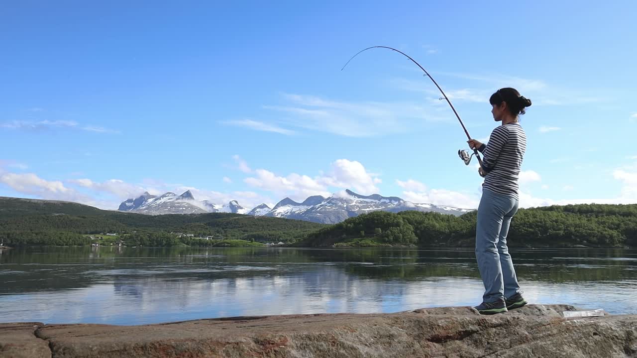 Seorang wanita menangkap ikan besar dengan joran pancing dan tidak bisa menariknya keluar dari air. Memancing dengan joran pancing di Norwegia. Memancing di Norwegia adalah cara untuk merangkul gaya hidup lokal.