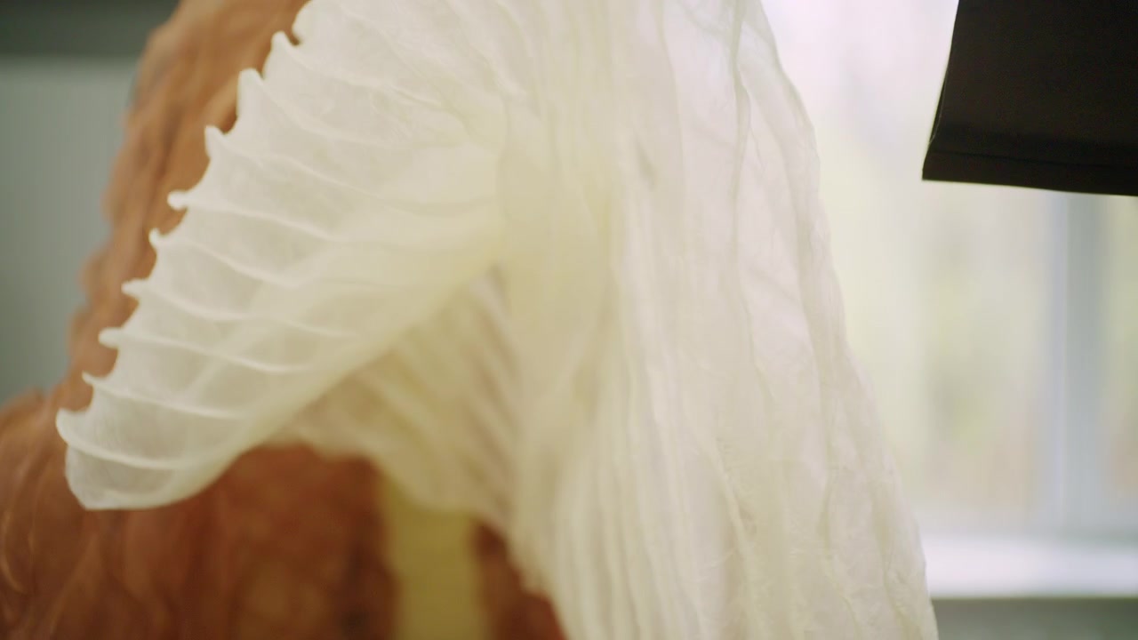 Scatto a fuoco morbido di un pannello di tessuto bianco testurizzato appeso davanti a organza trasparente arancione su un manichino da sartoria.
