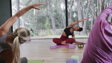 mujeres diversas estirándose juntas en esteras en la clase de yoga con una entrenadora femenina, cámara lenta