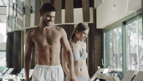 Smiling-couple-walking-indoor-pool.-Couple-resting-near-poolside.