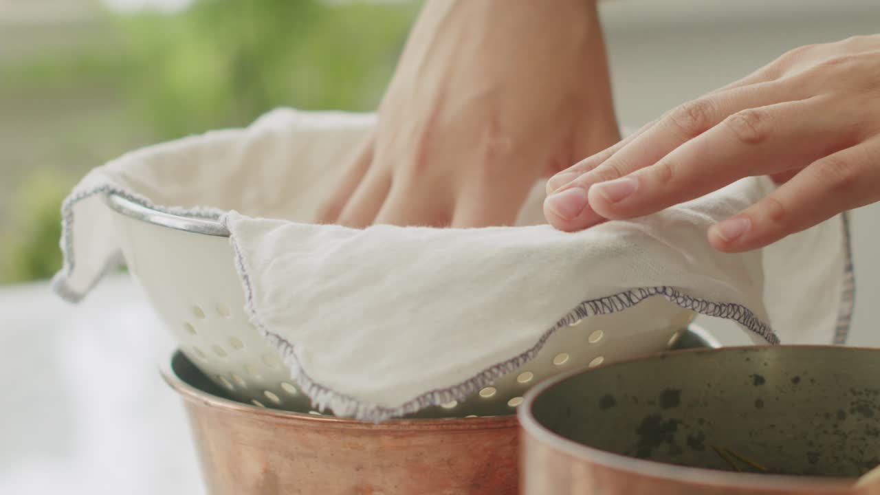 Crop woman putting napkin on strainer in kitchen