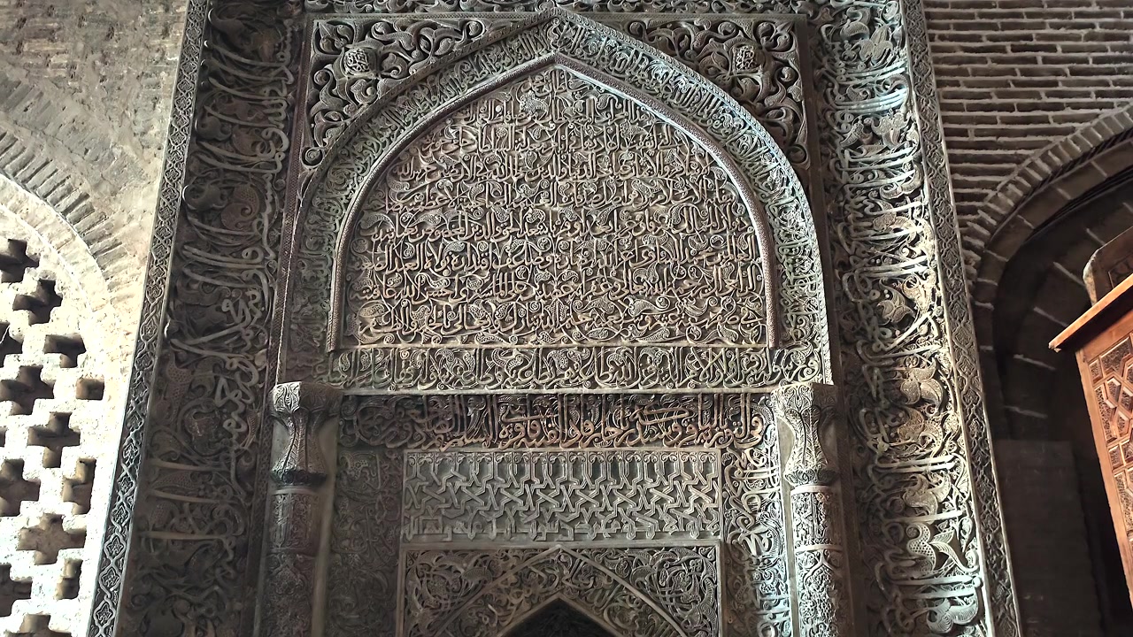 Intagli in pietra intricati e calligrafia araba su un'antica parete di moschea