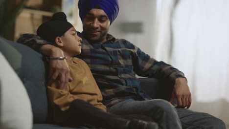 Padre-Sikh-Y-Su-Hijo-Con-Turbantes-Sentados-En-Un-Sofá-En-Casa-Hablando-Juntos,-Filmados-En-Tiempo-Real