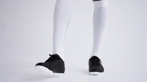 joven jugador de fútbol afroamericano está jugando con la pelota en el estudio de primer plano de los pies y de longitud completa