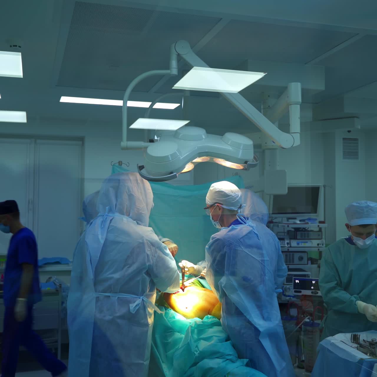 Surgery in the operating theater. Team of medical specialists in protective uniform conduct a surgery. Video shot through the window inside hospital.