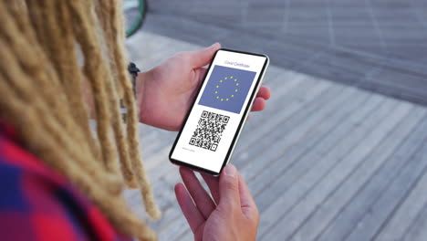 hombre con dreadlocks sosteniendo un teléfono inteligente, certificado de vacunación contra la covid, bandera de la ue y código qr en la pantalla