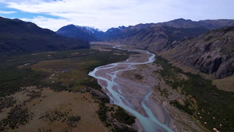 aerial drone footage showcases the stunning las vueltas river in argentina, featuring vibrant light blue waters, framed by lush green forests and majestic mountains on a cool summer day.