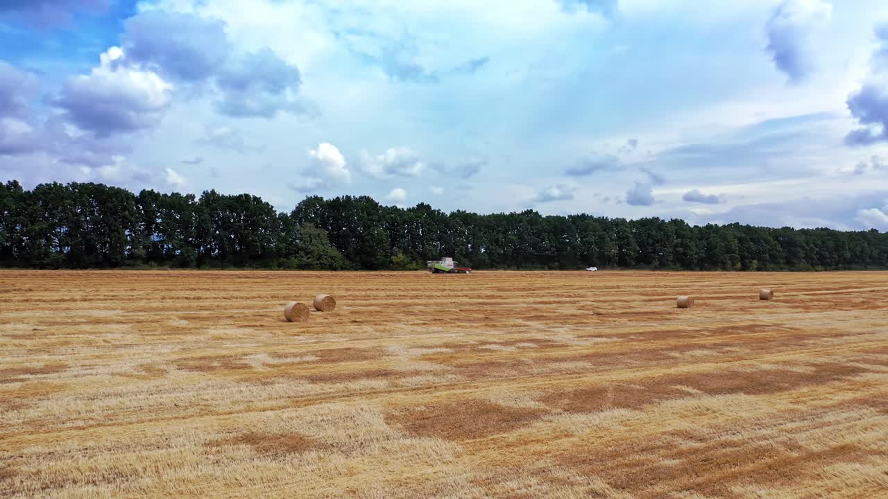 Golden field during seasonal works under blue sky. Natural landscape of a field and agricultural machine working in a daytime. Aerial view.