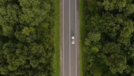 Seguimiento-Aéreo-De-Un-Dron-Que-Muestra-Un-Vehículo-Blanco-Circulando-Por-Una-Carretera-Asfaltada-En-Un-Bosque-De-Robles