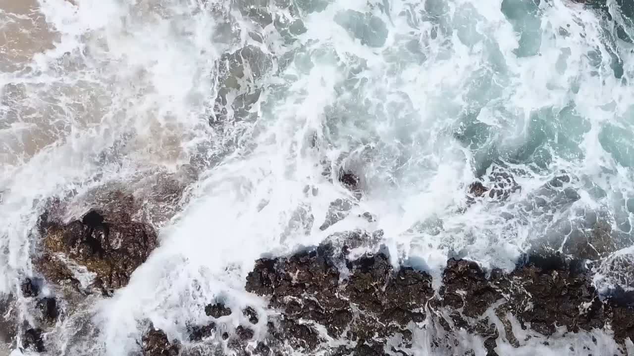 Ripresa aerea con drone: onde oceaniche si infrangono su scogli e spiaggia