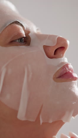 mujer suaviza la máscara de tela cosmética en la cara en el baño. mujer participa en procedimientos cosméticos agradables haciendo máscara facial después de un duro día de trabajo