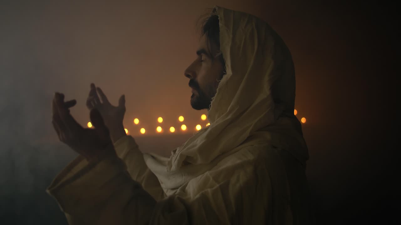 Closeup of Jesus Christ lifting his hands praying, worshipping in solemn, sacred moment for cinematic Christian stock footage