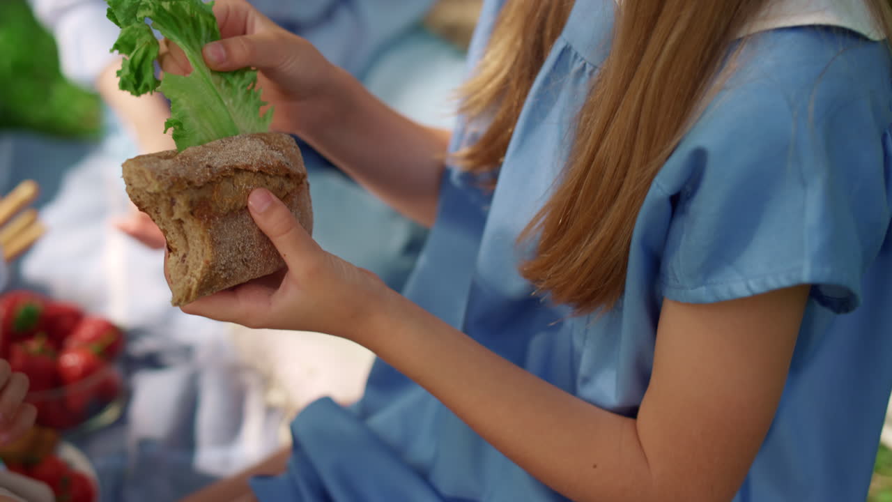 manos de chicas no reconocidas sosteniendo sándwiches de cerca. almuerzo familiar en la naturaleza.